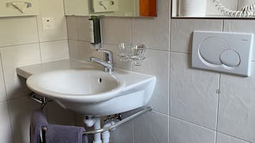 Un baño con lavamanos blanco, un espejo, toallero, inodoro y secador de pelo montado en la pared.