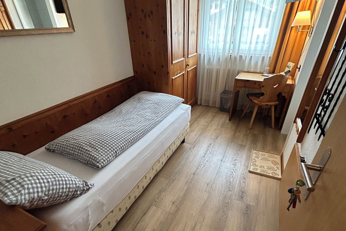 Ein kleiner, gemütlicher Raum mit einem Einzelbett, einem Schreibtisch und einem Stuhl.