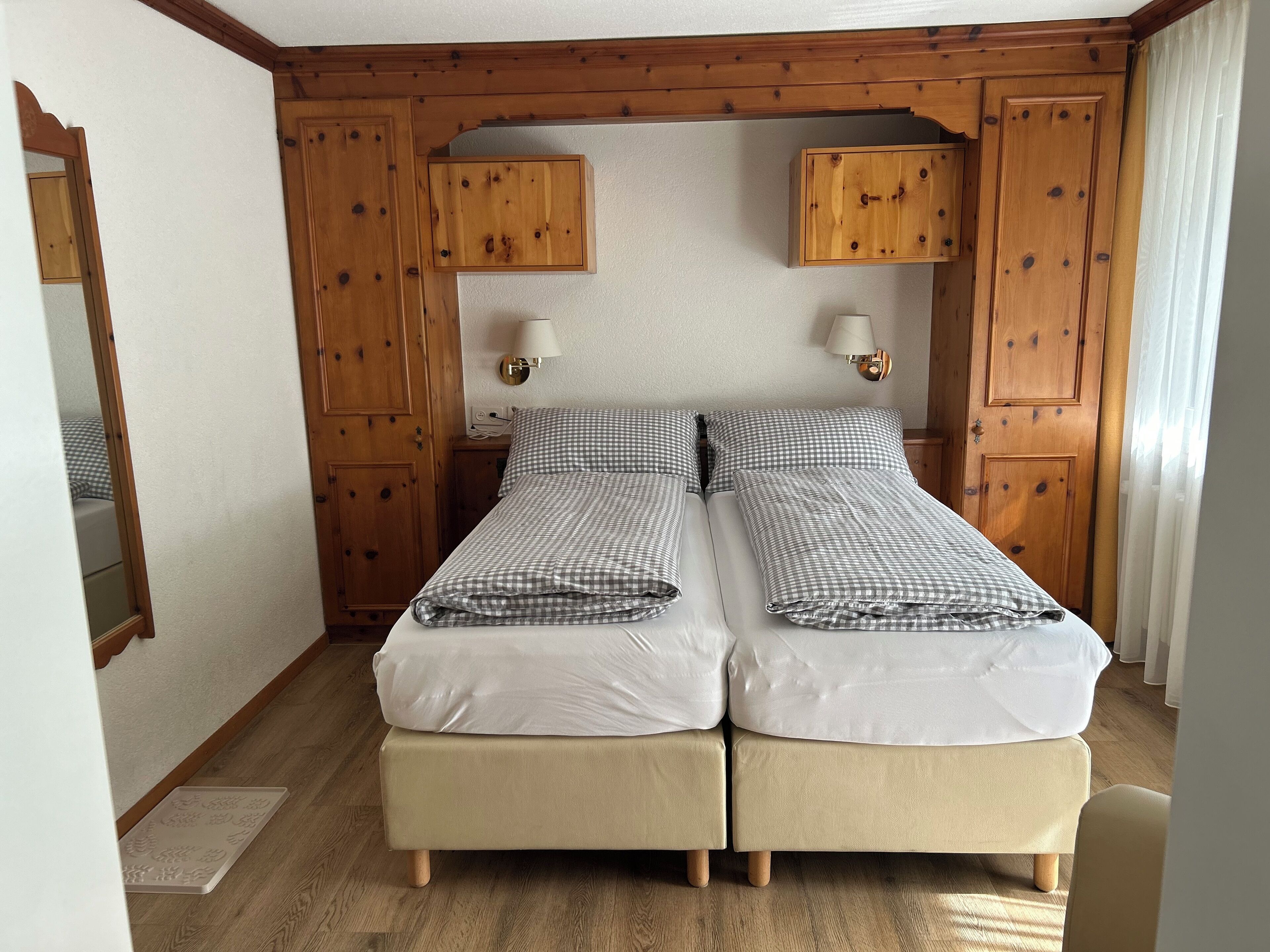 Un lit double avec une literie à carreaux, des panneaux de bois sur les murs et deux lampes fixées au mur.