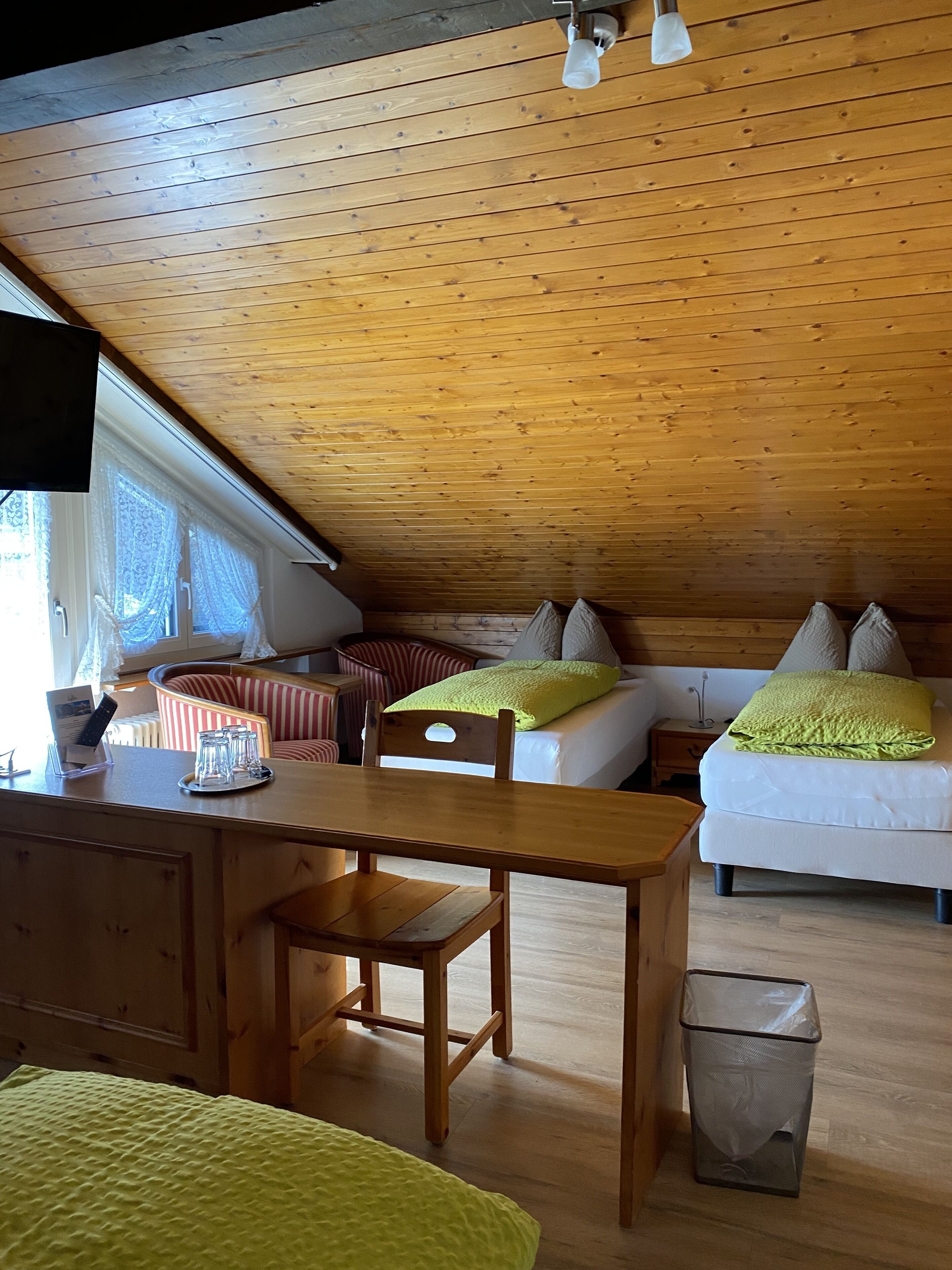 Una habitación acogedora con techo de madera, una cama con almohadas verdes, un sofá y una pequeña mesa con vasos y un control remoto.