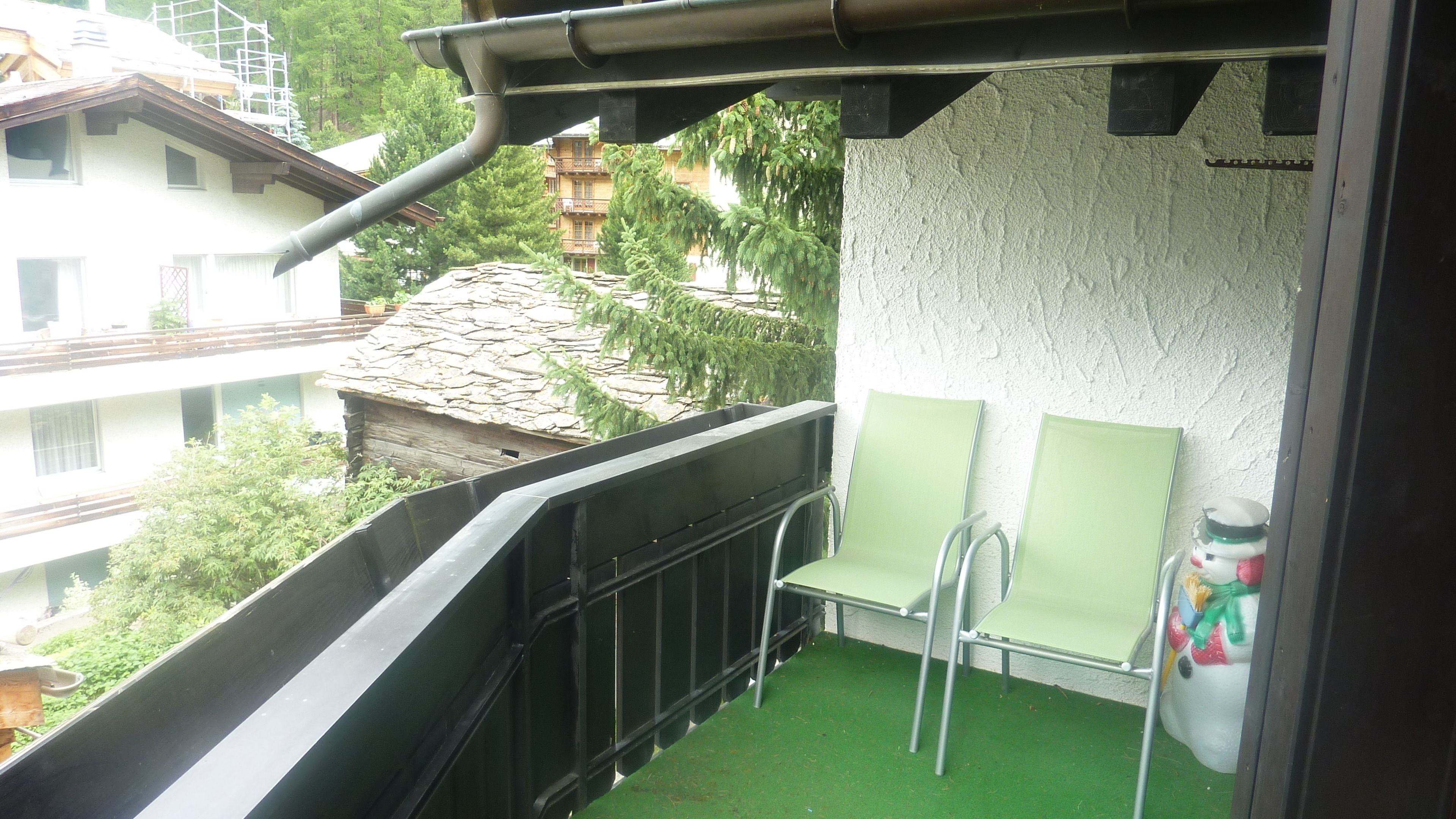 Un balcone con un pavimento in erba sintetica verde, due sedie verdi e un tavolino.
