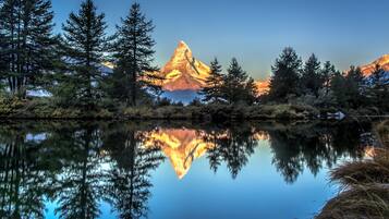 Une montagne se reflète dans un lac paisible, entouré d’arbres.