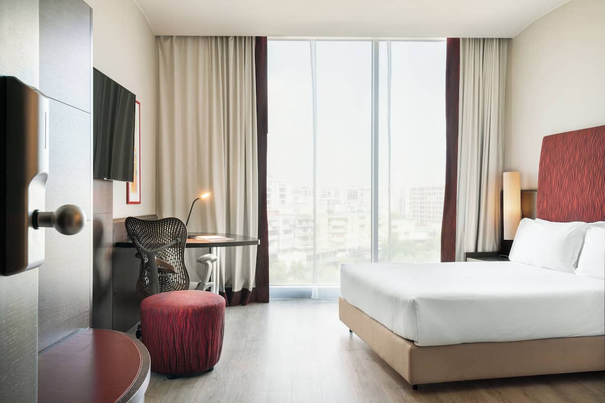 A hotel room with a bed, a desk, a chair, a TV, and a view of the city.