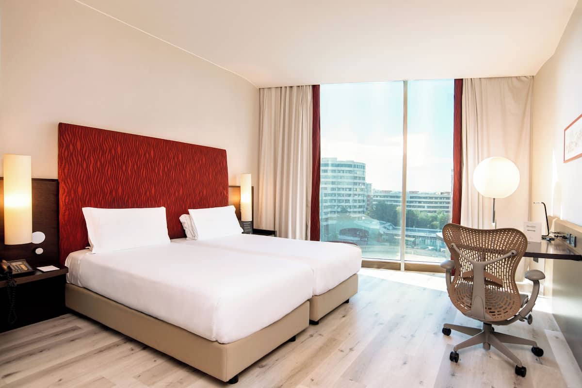 A hotel room with a large bed, a desk, a chair, and a view of the city.