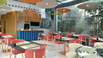 Um restaurante moderno com cadeiras vermelhas e bege, mesas pretas e um balcão central.