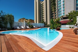 Una piscina con cubierta de madera, rodeada de sillas de descanso y plantas en macetas.