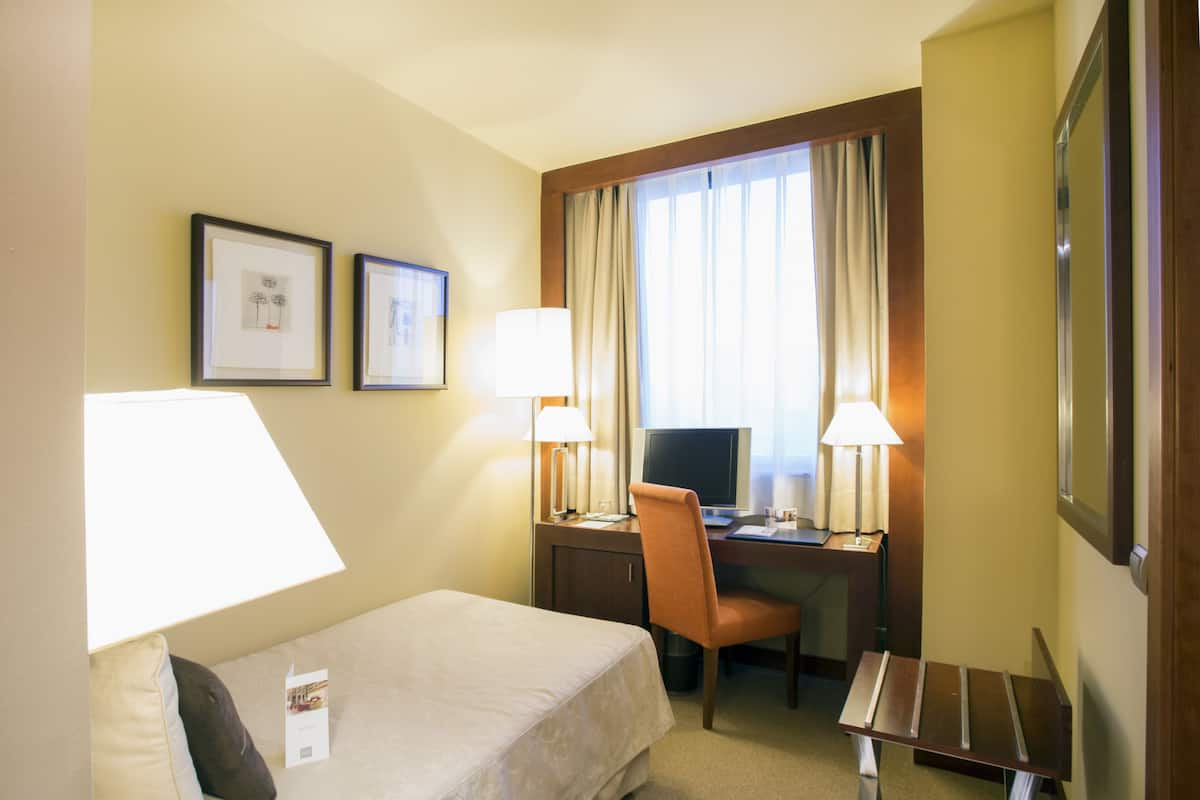Une chambre d’hôtel avec un lit, un bureau, une chaise et deux lampes.