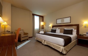 A hotel room with a large bed, two bedside lamps, a desk with a lamp, a chair, and a window with curtains. - Nuevo Madrid (Madrid)