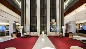 Um hall amplo com um tapete vermelho central, dois sofás um de frente para o outro e um balcão de recepção moderno.
