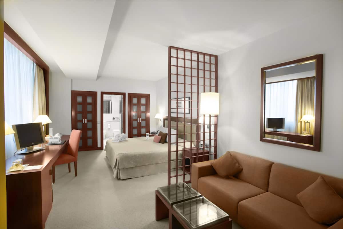 Une chambre d’hôtel équipée d’un bureau, d’une chaise, d’un lit, d’un canapé et d’une cloison.