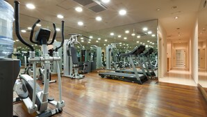 Uma academia com diversos equipamentos de exercícios, um bebedouro e um espelho grande na parede.