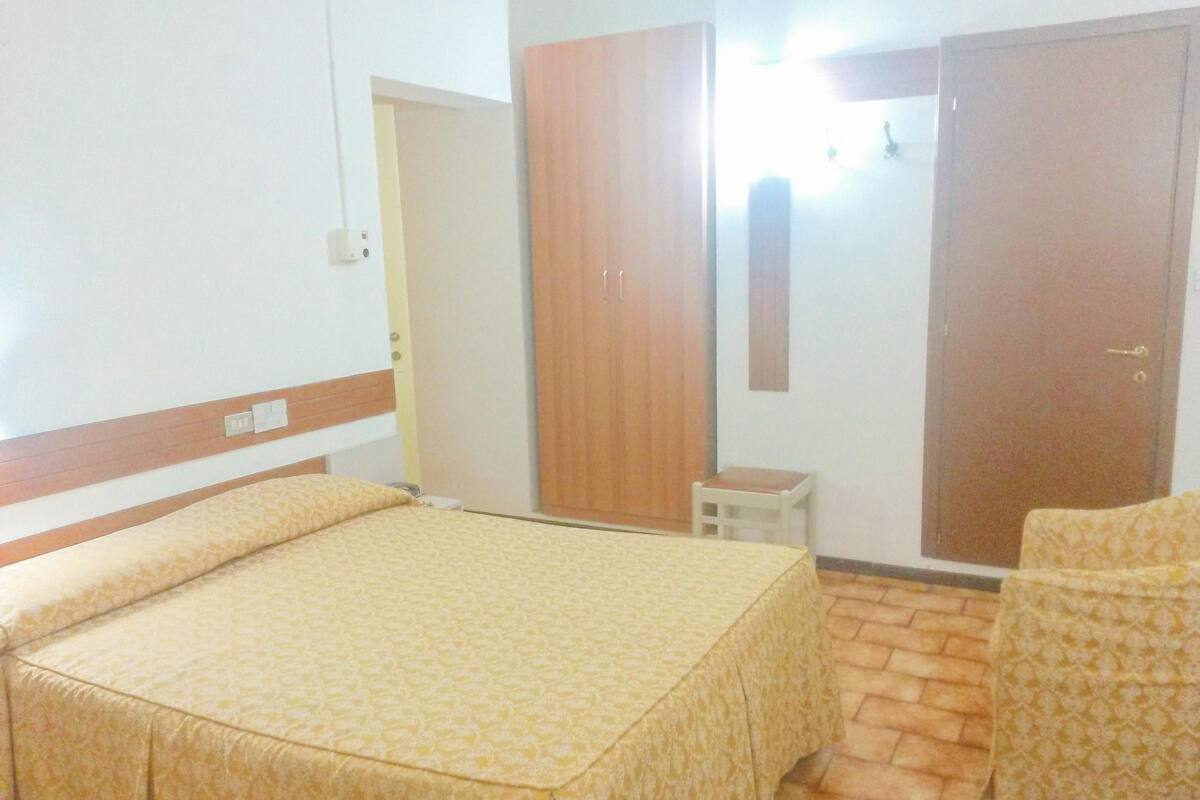 Une chambre d’hôtel avec un lit, deux chaises, une petite table et une armoire.