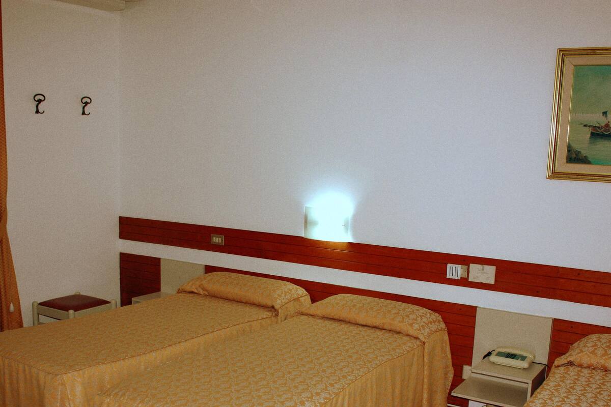 Une chambre d’hôtel avec deux lits, une table de chevet, une lampe, un tableau et une fenêtre avec des rideaux.