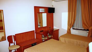 Habitación de hotel con un escritorio de madera, dos camas individuales, una silla, un espejo y una ventana con cortinas.