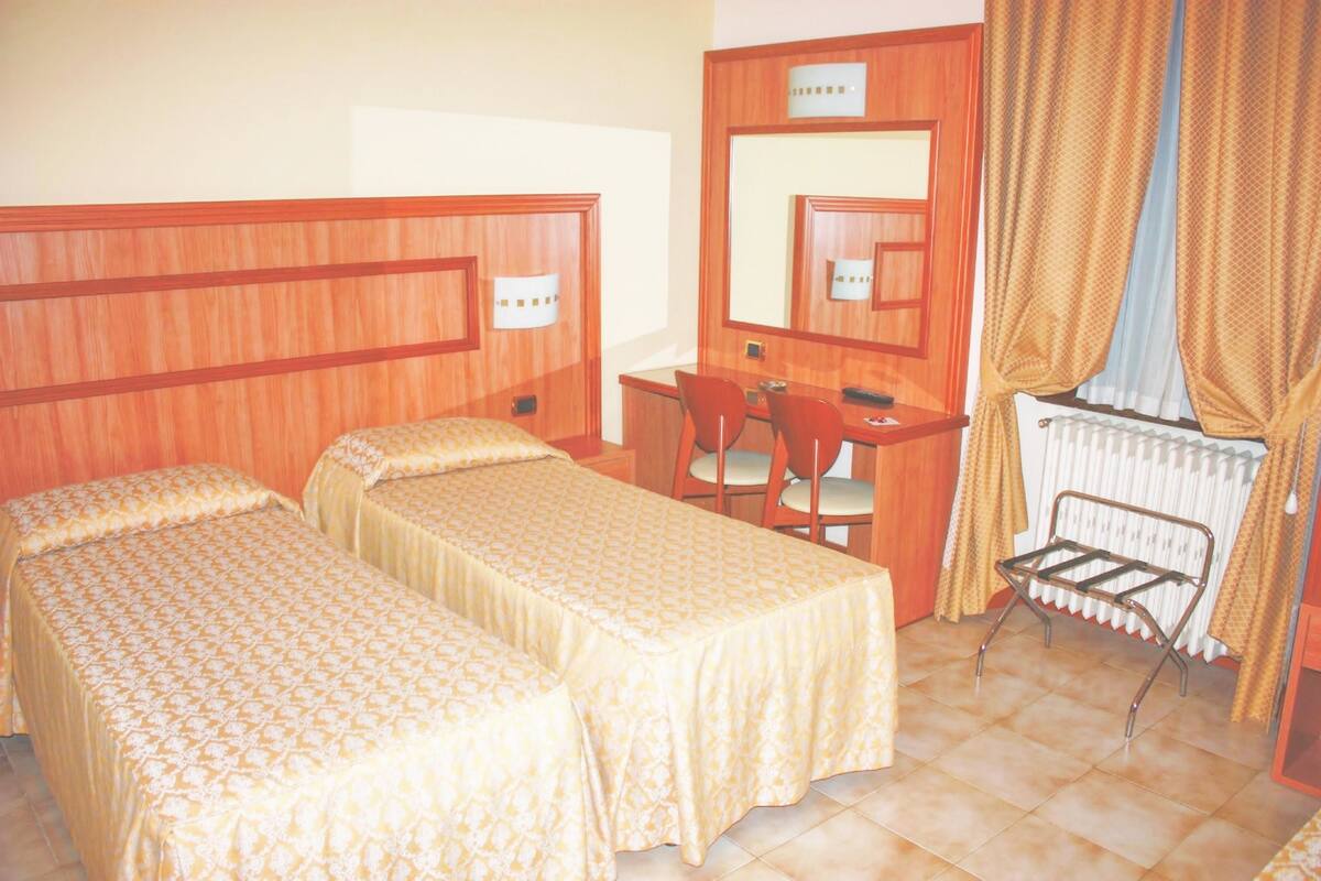 Une chambre d’hôtel avec deux lits simples, un bureau, une chaise et un radiateur.
