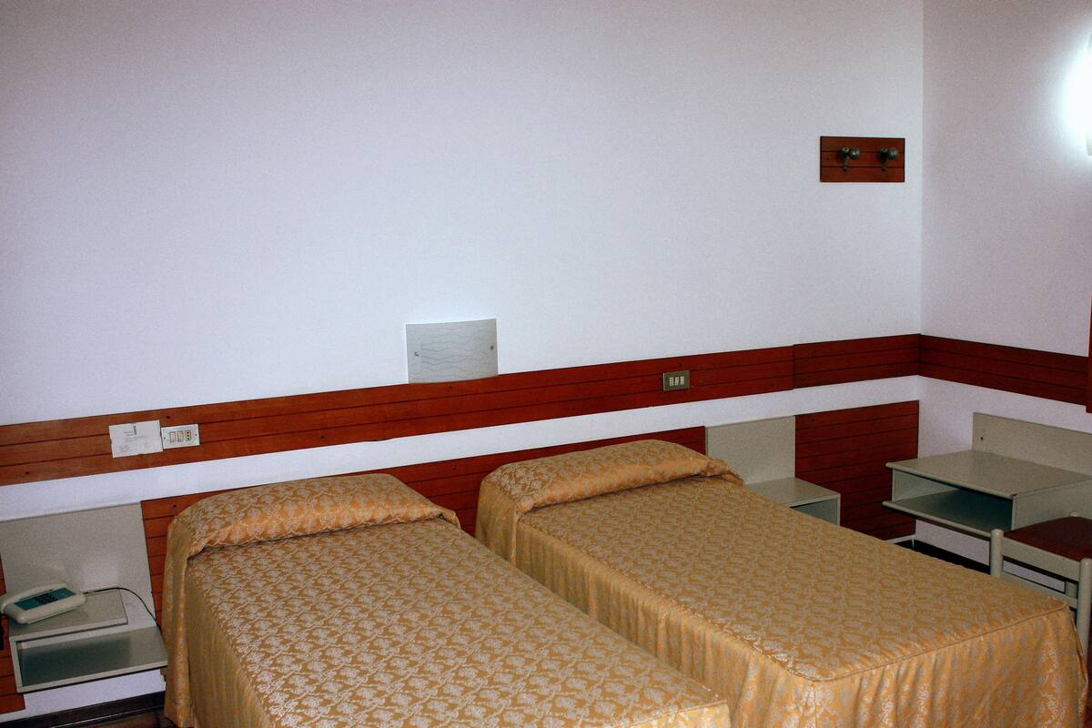 Une chambre d’hôtel avec deux lits simples, un bureau, une chaise et un miroir.