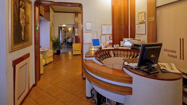 A hotel reception area with a curved desk, a computer, and a clock on the wall. - Piccolo Hotel (Milan)