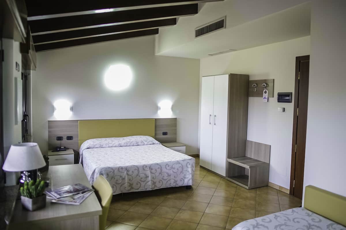 A hotel room with two beds, a desk with a lamp, a small table with a plant, and a wardrobe.