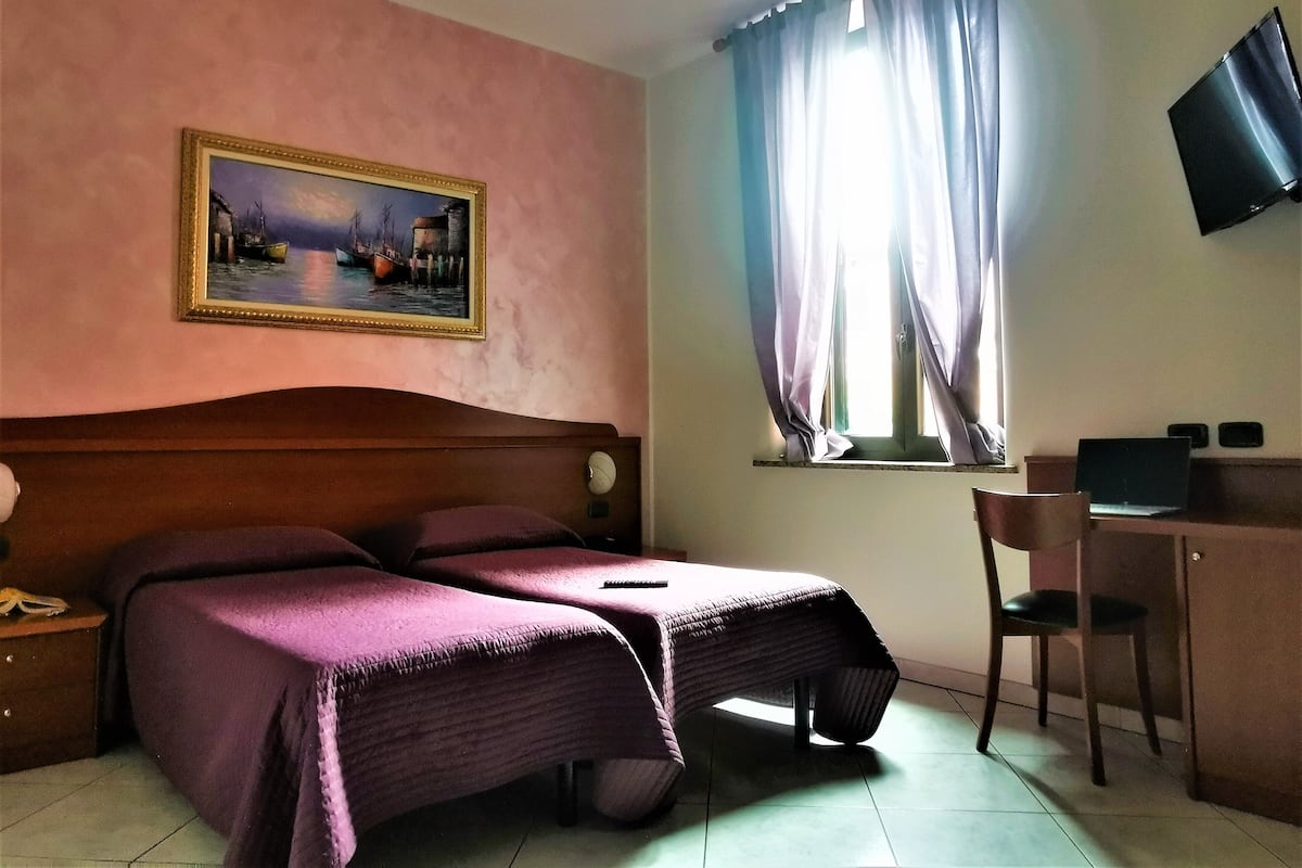 A bedroom with a bed, a desk, a chair, a television, and a painting on the wall.