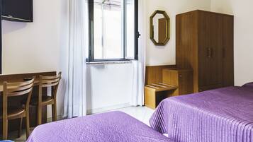 Habitación de hotel con dos camas, un escritorio con sillas, un armario y una televisión en la pared.