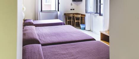 Habitación tipo dormitorio con dos camas, un televisor montado en la pared, una mesita con sillas y una ventana con cortinas.