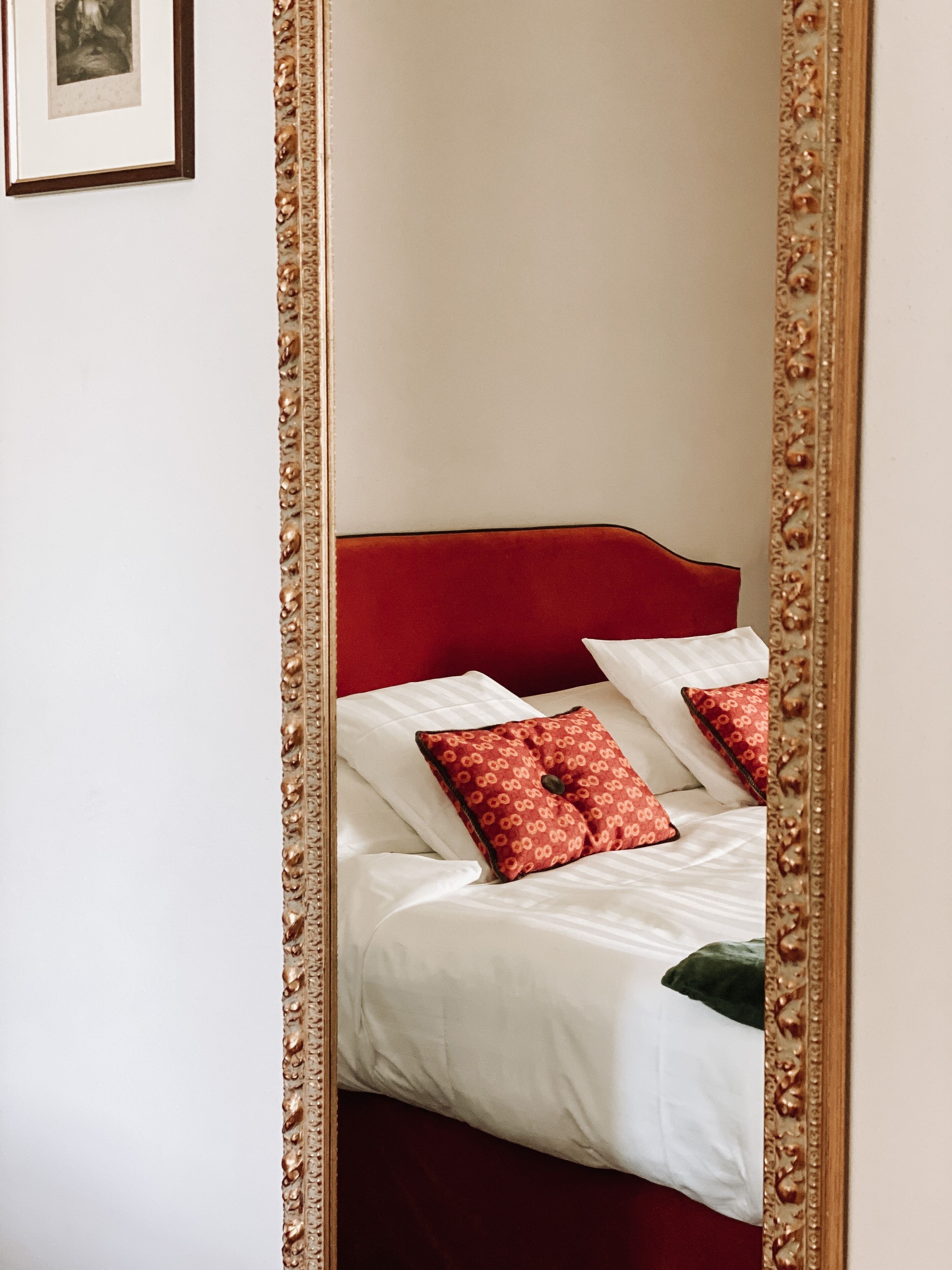 Un letto con lenzuola bianche e cuscini rossi, una testiera rossa e uno specchio con cornice elaborata.