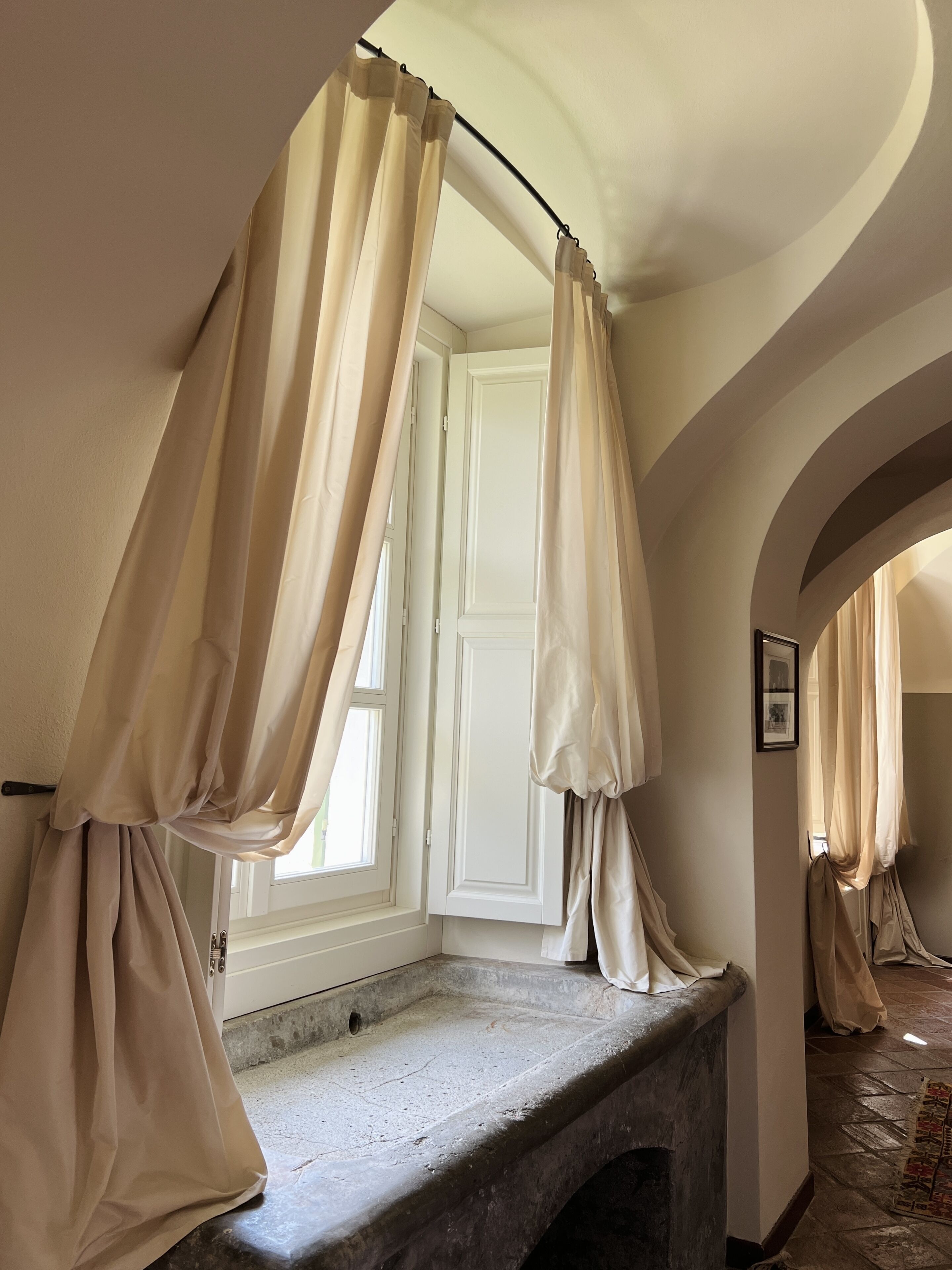 Una habitación con un banco de piedra, una puerta blanca y cortinas color beige.