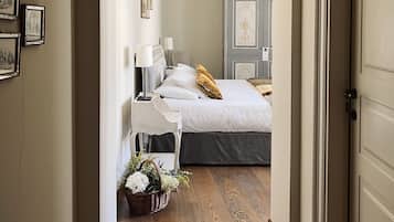 Un pasillo que conduce a un dormitorio con cama, mesitas de noche y un velador.