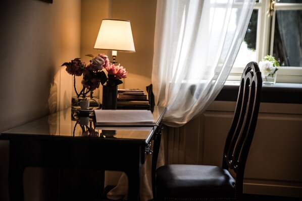 Una habitación con escritorio, una silla, una lámpara y una ventana con cortinas.