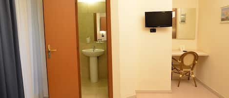 A hotel room with two beds, a bathroom with a sink, a chair, a desk, and a TV mounted on the wall.