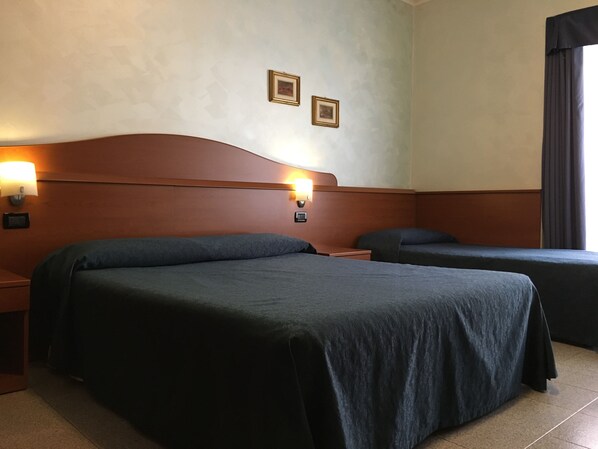 Una habitación de hotel con dos camas, cabeceros de madera, lámparas de pared y un ventanal con cortinas.