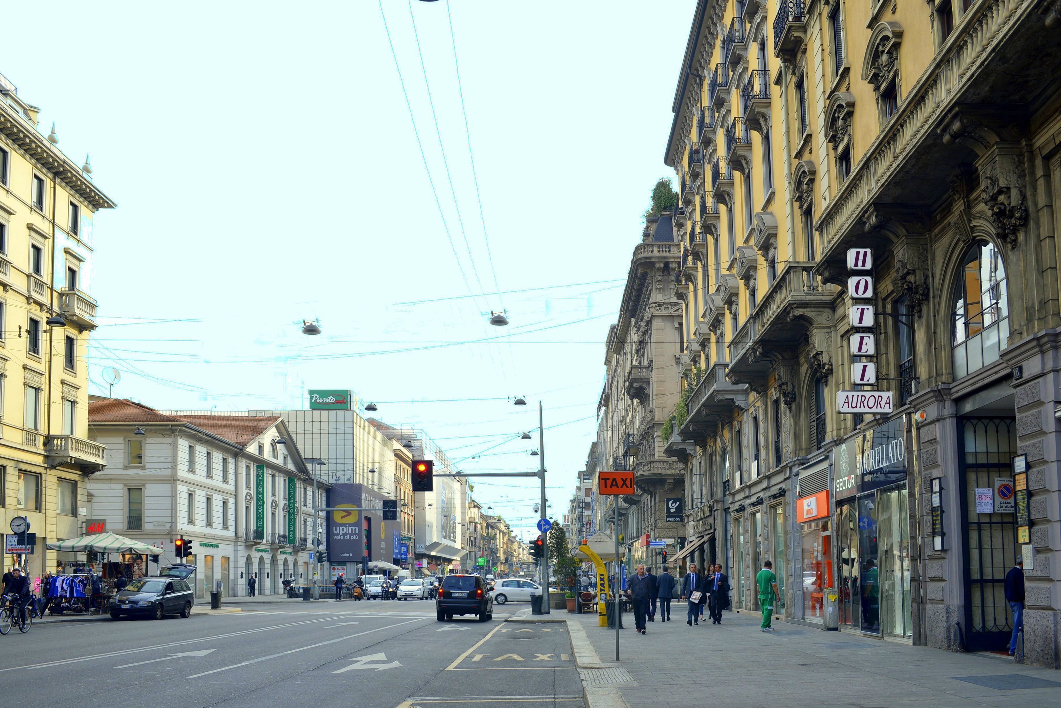 Straßenansicht mit einem Hotel namens "Aurora" auf der rechten Seite, mit einem Schild, das den Namen des Hotels zeigt.