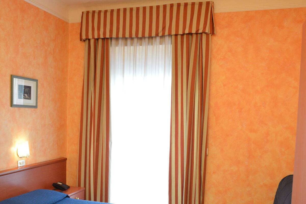A hotel room with a large bed, a desk, a chair, and a window with curtains.