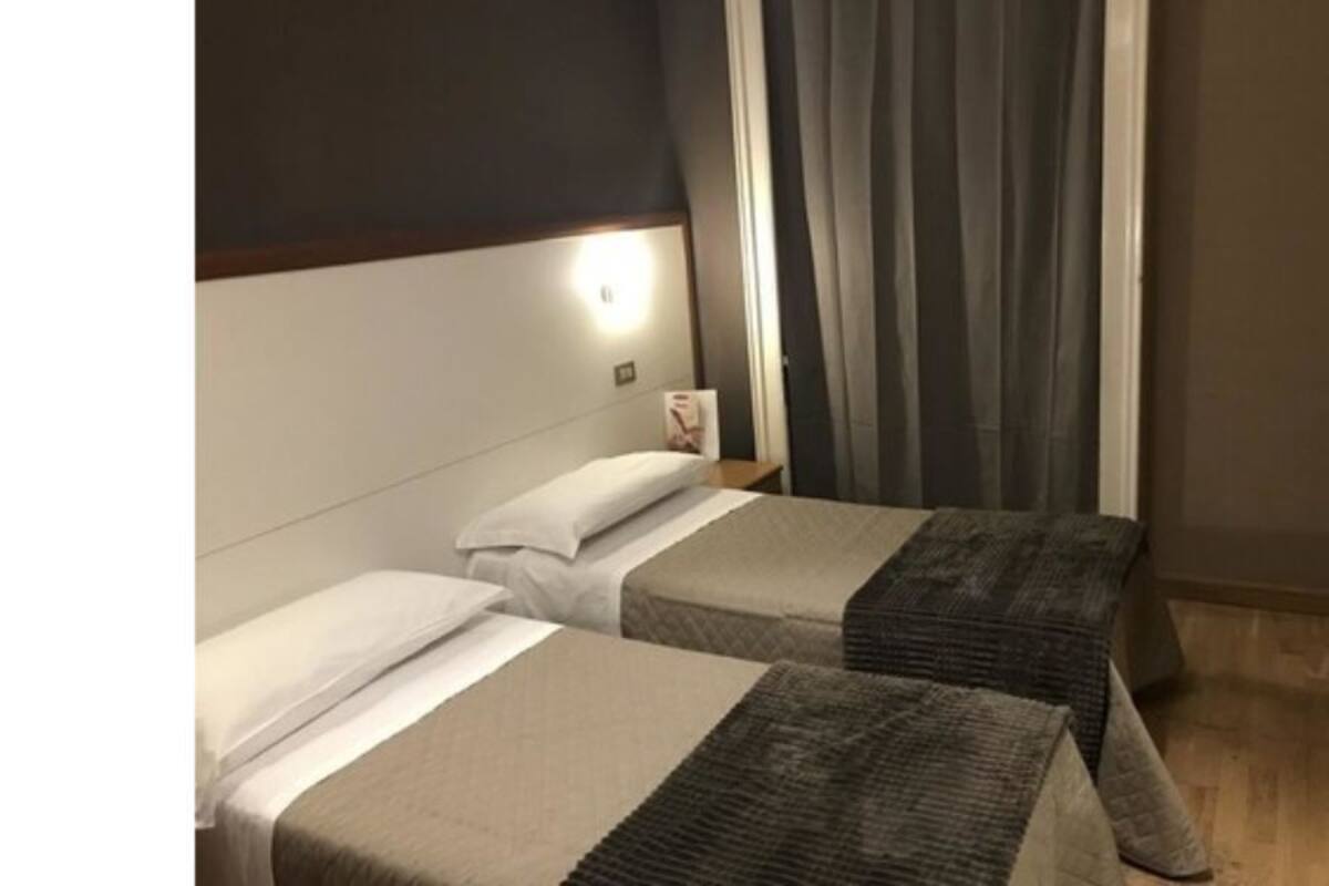 A hotel room with two beds, a nightstand, and a window with curtains.