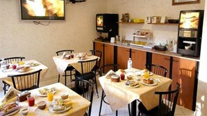 A dining area with tables set for breakfast, a television mounted on the wall, and a kitchen counter with appliances. - Hotel Bogart (Milan)