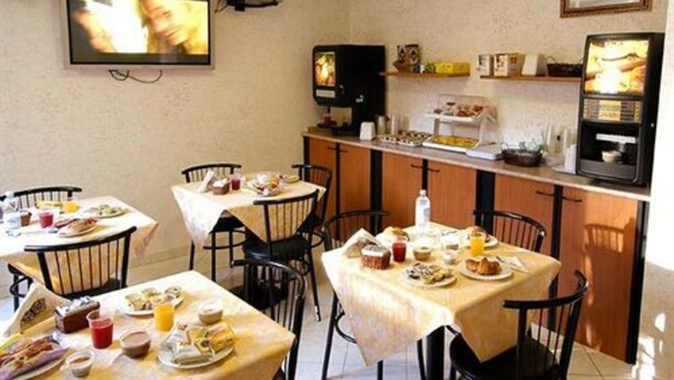 A dining area with tables set for breakfast, a television mounted on the wall, and a kitchen counter with appliances. - Hotel Bogart (Milan)