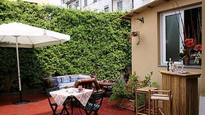 An outdoor patio with a table and chairs, a white umbrella, and a wooden bar. - Hotel Bogart (Milan)