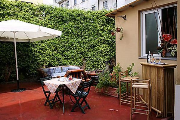 An outdoor patio with a table and chairs, a white umbrella, and a wooden bar. - Hotel Bogart (Milan)