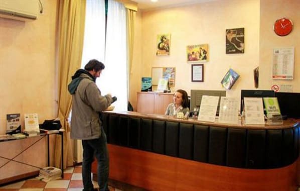 A reception desk with a counter, a clock, and a few framed pictures on the wall. - Hotel Bogart (Milan)