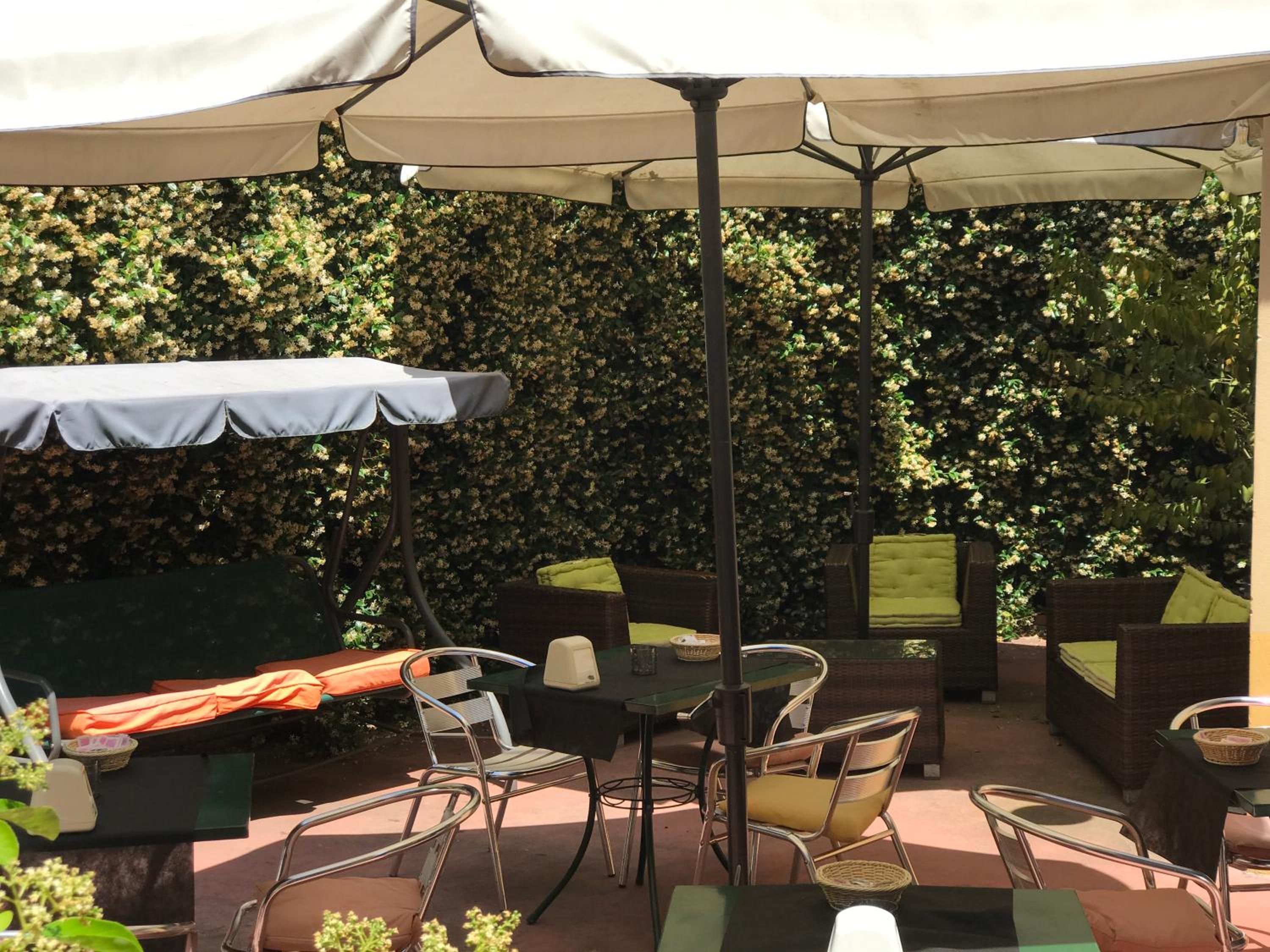 Un'area patio esterna con tavoli e sedie, circondata da un siepe.