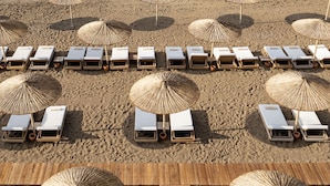 A beach with rows of sun loungers and thatched umbrellas, arranged in a neat pattern. - Titanic Deluxe Lara - All inclusive (Antalya)
