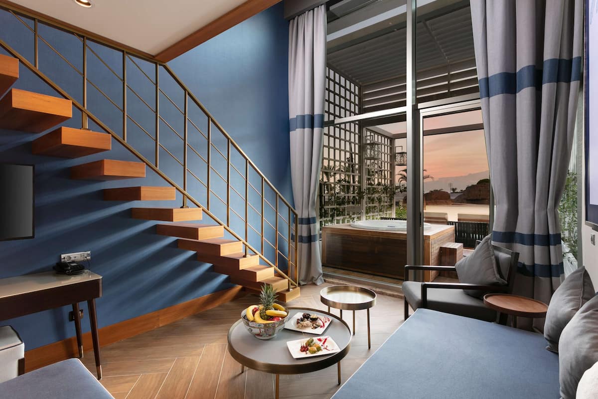 Uma sala de estar moderna com escada, área de jantar com mesa e cadeiras, e vista para o exterior.