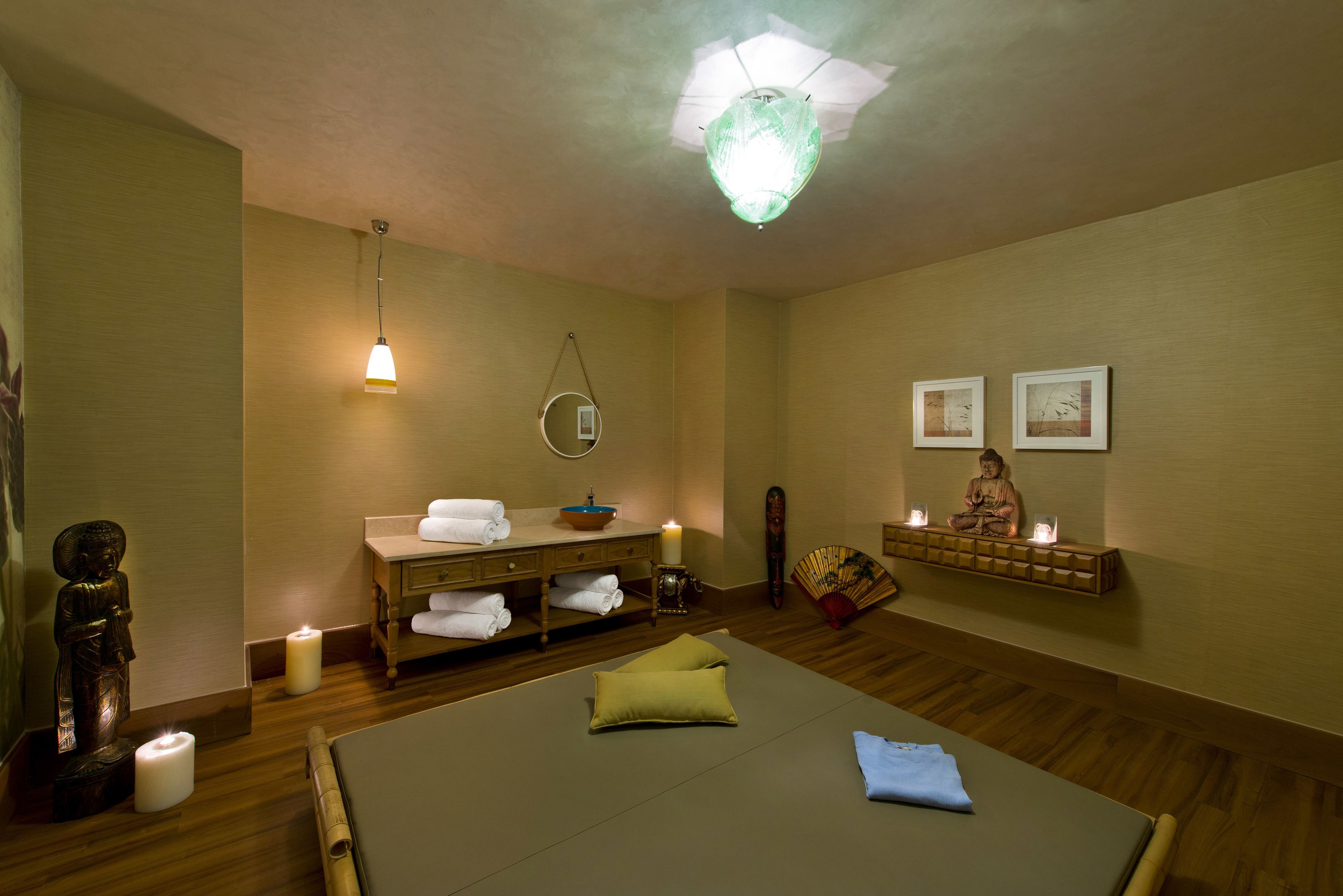 Ein Spa-Raum mit Massagetisch, Kerzen, einer Statue, einem Spiegel und einem Regal mit Bildern.