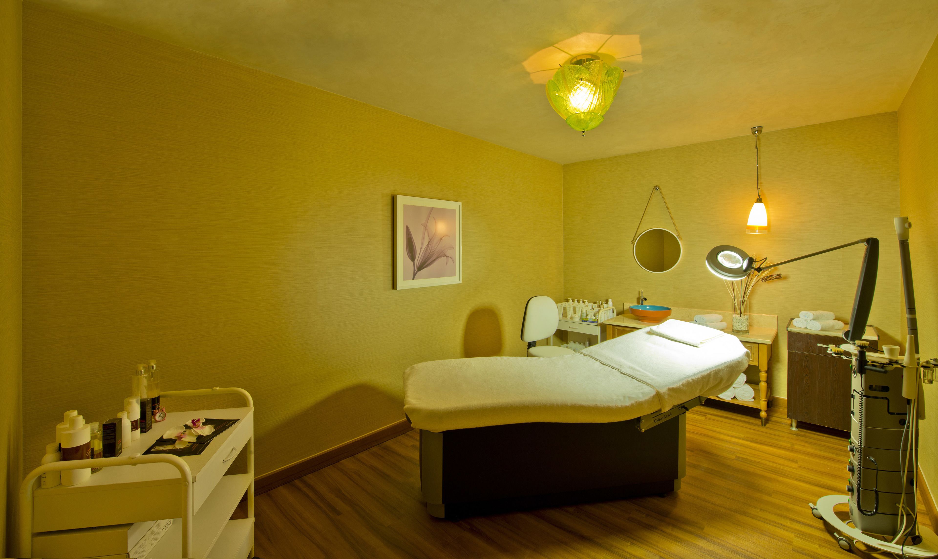 Ein Zimmer mit einem Bett, einem kleinen Schreibtisch mit Stuhl, einem Spiegel, einer Lampe und einem Regal mit Toilettenartikeln.