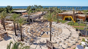 A resort with a circular outdoor seating area, palm trees, and a view of the sea. - Titanic Deluxe Lara - All inclusive (Antalya)