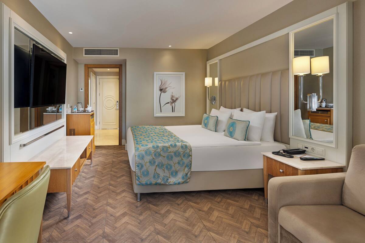 Quarto de hotel com cama, mesa de cabeceira, televisão e espelho.