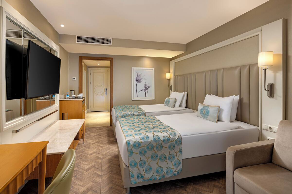 Quarto de hotel com duas camas, televisão, escrivaninha e uma cadeira.