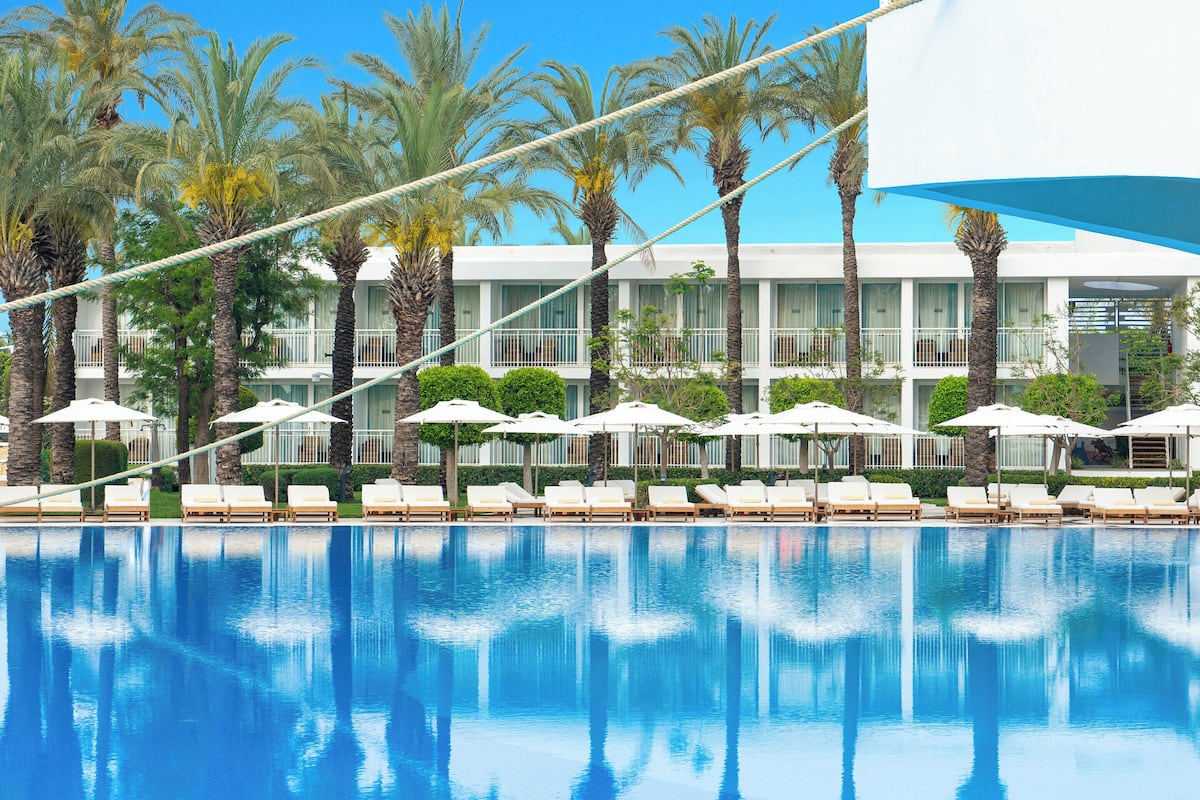 Um hotel com piscina, palmeiras e guarda-sóis brancos.