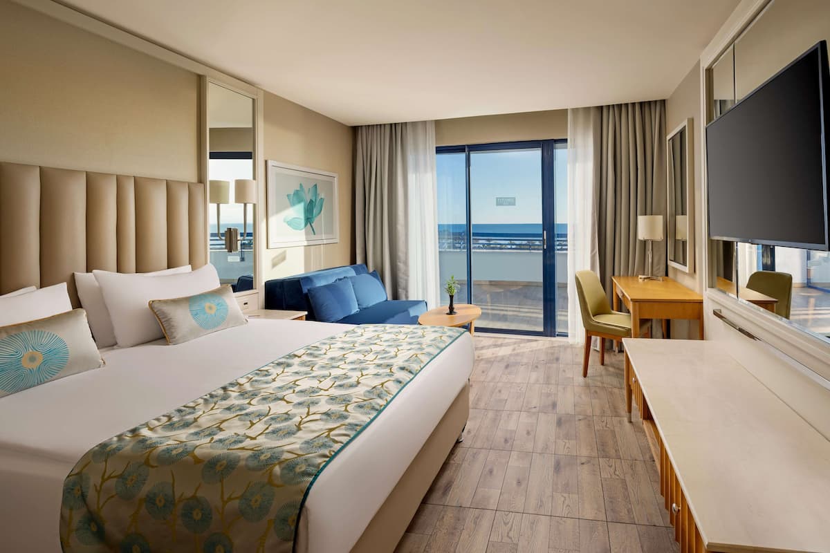 Quarto de hotel com uma cama grande, um sofá, uma mesa de jantar e vista para o oceano.
