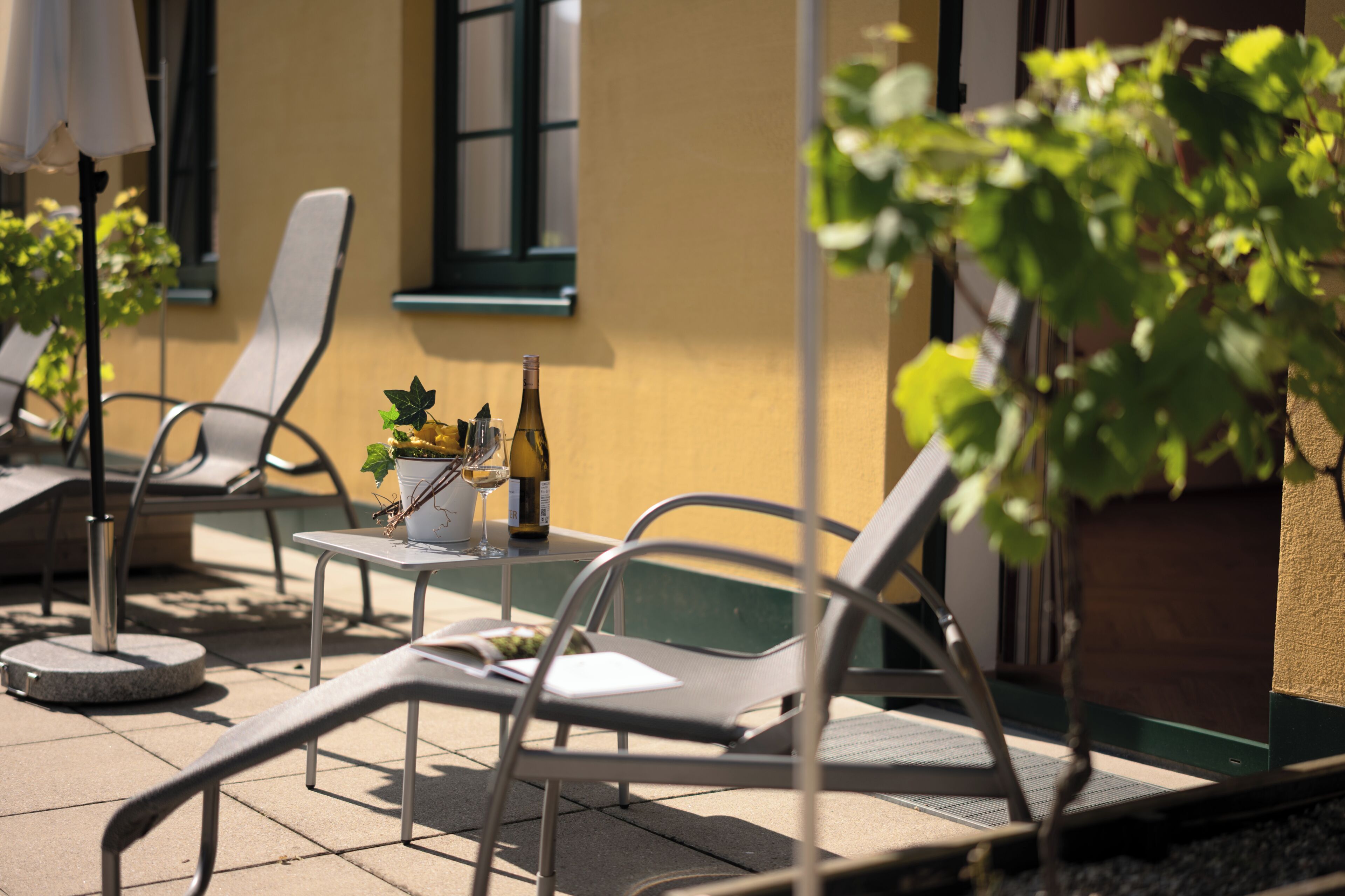 An outdoor seating area with metal chairs, a table with a bottle and glasses, and a potted plant.